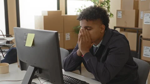 Man covering face with hands at computer amid parcel boxes in a building; s.. Stock Footage 337418319