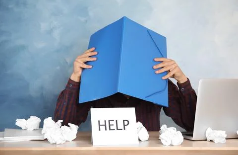 Man covering head with folder at table in office. Asking for help 스톡 사진