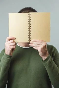 The man covers his face with a notebook. Vertical image Stock Photos