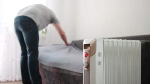 A man covers a sofa with a blanket against the backdrop of an electric heater Stock-Footage 253470037