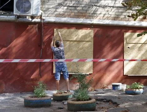 A man covers windows broken after a rocket attack with plywood. Stock-Fotos