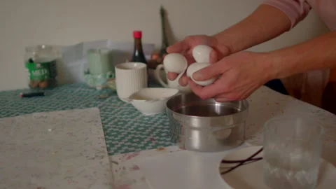 Man cracking eggs over saucepan with rustic surroundings during morning cooking Stock Footage 325072560
