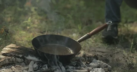 Man cracks egg into frying pan on campfire Stock Footage 76703600