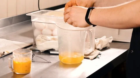 Man cracks white eggs into measuring cup in pro kitchen Stock Footage 107599364