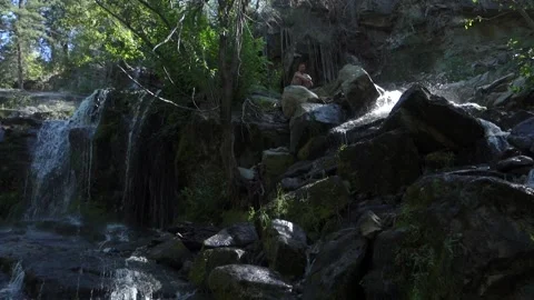 Man Crawls Over Rocks Above Waterfalls with Shining Sun Stock Footage 232050895