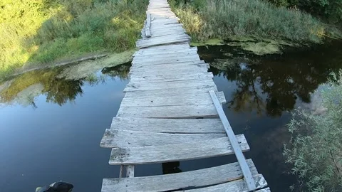 A man crosses a suspension bridge without railings over a river. He points wi Vídeos de archivo 145967623