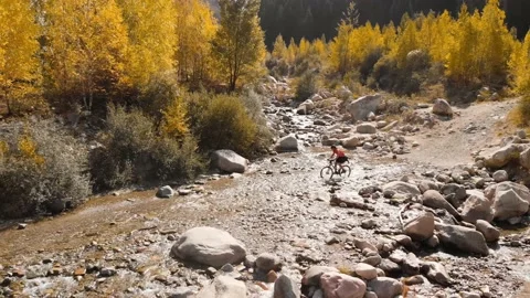 Man is crossing the river by bicycle in the mountains shot by drone 库存影片 139956746