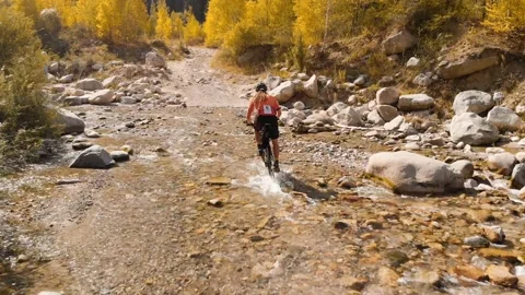 Man is crossing the river by bicycle in the mountains shot by drone Vidéo 139956843