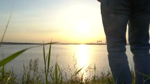 Man crouched down on grass and admired beautiful sunset on river. Видео 155863427
