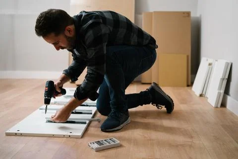 Man crouched on the floor assembling a piece of furniture. Do it yourself Stock Photos