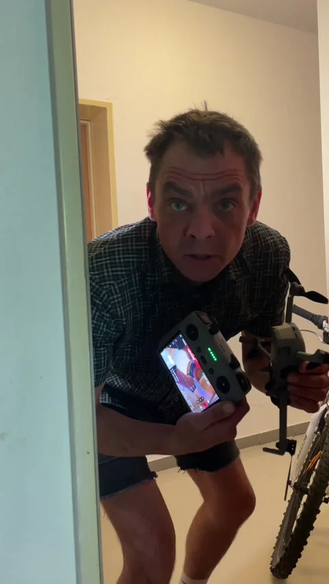 Man crouched in hallway holding drone and remote controller with focused gaze Видео 344584463