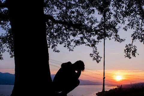 Man crouching under the tree and silhouette of the tree. sad mood. Stock Photos