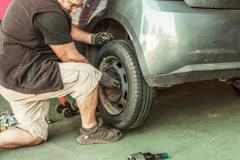Man crouching while putting on a wheel from a car in a workshop Stock Photos