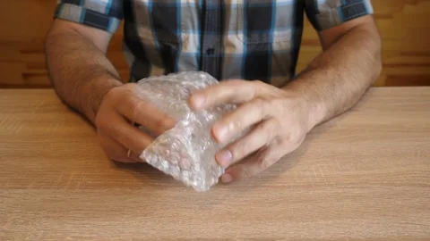 A man crumples bubble wrap in his hands, creating a distinctive crackling sou Stock Footage 341254560