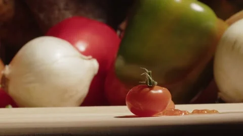 A man crushes a fresh cherry tomato with a knife. Cooker preparing vegetarian Stock Footage 229642303