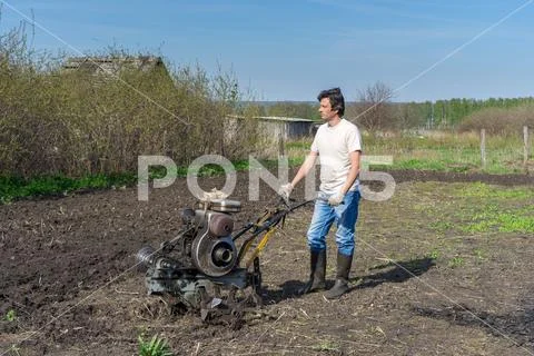 Man with cultivator ploughs ground. Land cultivation, soil tillage. Spring wo Stock Photos