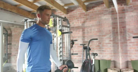 Man curling hex dumbbell in home gym to build strength, camera shifting front to Video stock 337294994