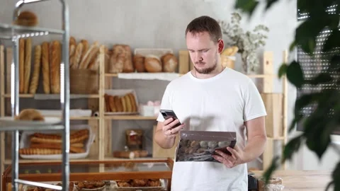 Man customer at bakery scans QR code on cookie package using phone camera Stock Footage 322116482