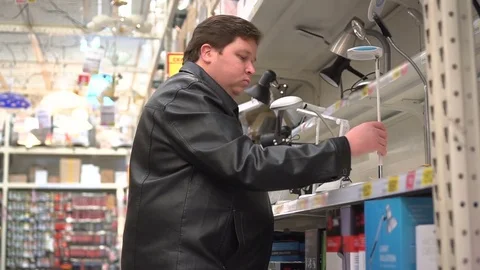 Man customer in the shop looking table lamp. Choosing a reading lamp for the Stock Footage 84140065