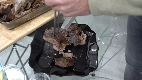 A man cuts and puts on plates pieces of hot fried duck from a black dish  Video stock 125400258