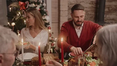 Man cuts and serves chicken on the table on Christmas Eve, everybody chatting 스톡 동영상 164688030