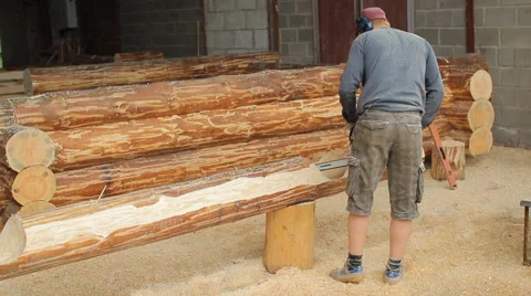 Man cuts off beam chainsaw for future log cabin. Construction works with a Stock Footage 65205626