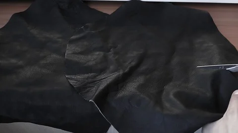Man cuts black leather with scissors for tailoring Stockbeeldmateriaal 129612829
