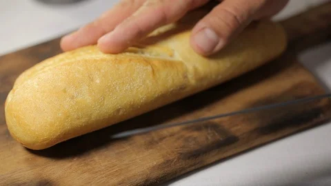 Man cuts bread h in a half by sharp knife on a wooden board at the kitchen 스톡 동영상 122010282