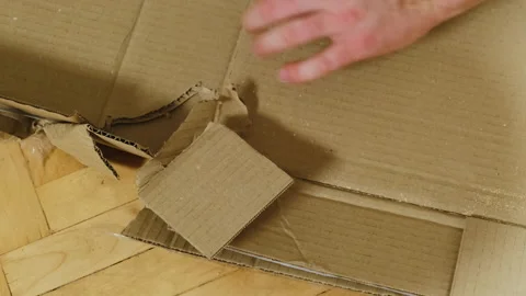 Man cuts cardboard box side sheets with knife on floor closeup Stock Footage 304399190