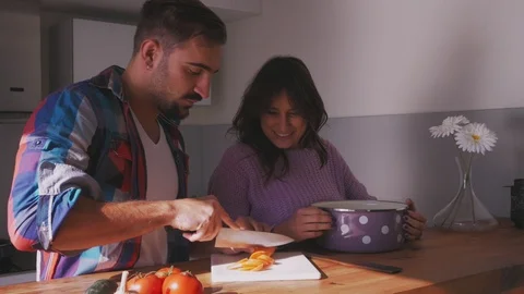 Man cuts carrot while girlfriend is smiling in the kitchen Stock-Footage 97642970