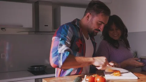 Man cuts carrot while girlfriend is smiling in the kitchen Stock-Footage 97644126