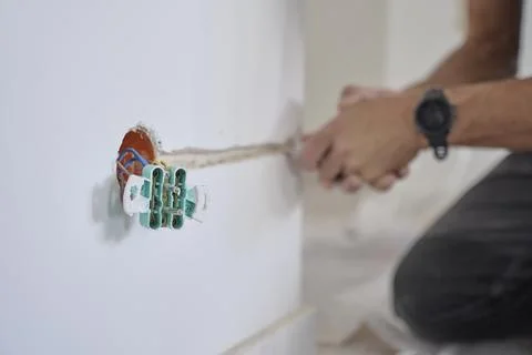 Man cuts channel in wall for electrical wire near exposed outlet Stock Photos