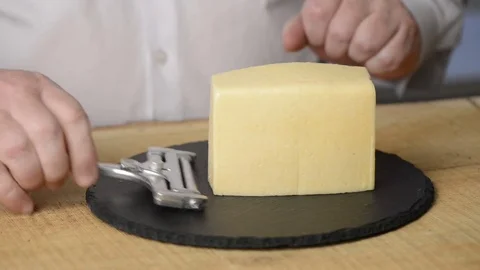 The man cuts cheese into thin slices with use of a cheese slicer on a black Stock Footage 78041561