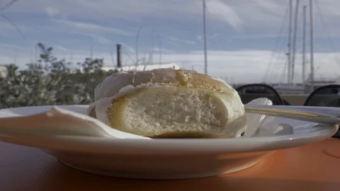 Man cuts a cinnamon bun in half at a harbour cafe in slomo Stock Footage 96889879