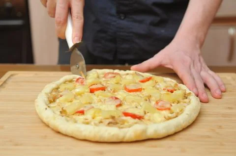 The man cuts the cooked pizza on the table in the kitchen, hands close up Stock Photos