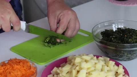 A man cuts dill on a cutting board. Nearby are potatoes, carrots and sorrel.  Stock Footage 136253534