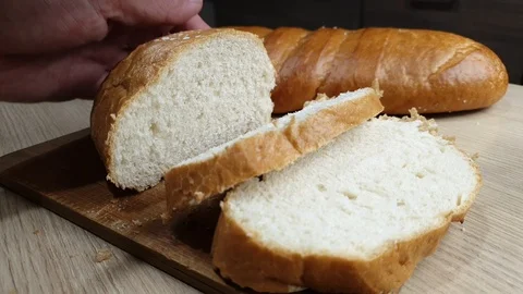 A man cuts fresh bread with a knife on a wooden Board in the kitchen Stock Footage 117588229