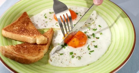Man cuts fried eggs with a knife on a green plate. close-up. angle view. Video stock 244295226