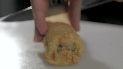 Man cuts a fried sushi roll with a knife. Roll lies on a board. Close-up. Stock Footage 87233315