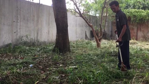 A man cuts the grass in the yard because it is tall and thick 스톡 동영상 274326095