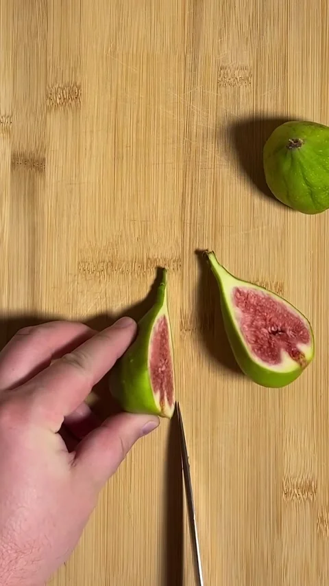 Man cuts green figs on gray plate on wooden cutting board Video stock 278683893