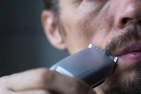A man cuts his beard and mustache with an electric razor, time to shave, bear Foto stock