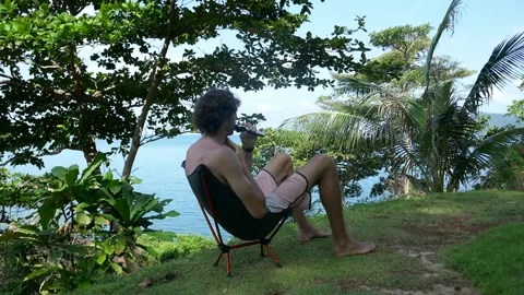 A man cuts his beard in nature at a campsite with a view of the sea Stock Footage 293273386