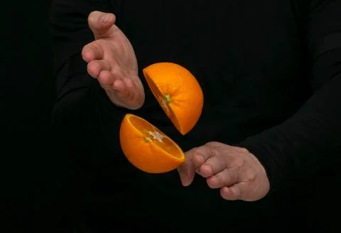 Man cuts an orange into two halves with his hands Stock Photos