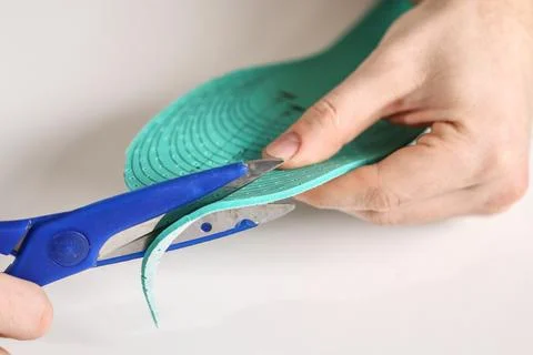 Man cuts out new shoe insoles with scissors to fit his foot size. Stock Photos