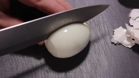 A man cuts a peeled chicken egg with a knife on a gray cutting board Stock Footage 171037993