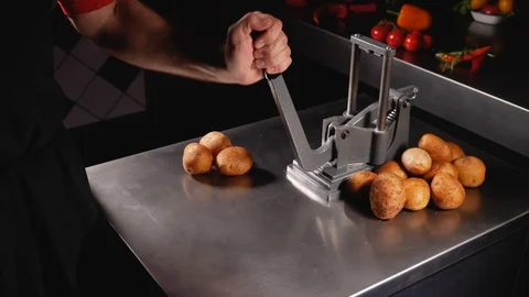 A man cuts peeled potatoes with a big french fries cutter. Slider shot. Stock Footage 128294384