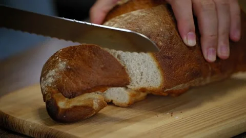A man cuts pieces of bread. Whole grain fresh bread on a wooden table. Stock Footage 201265595