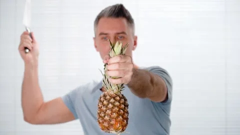 Man cuts pineapple in air holding it in one hand knife in other hand Stock Footage 147646750