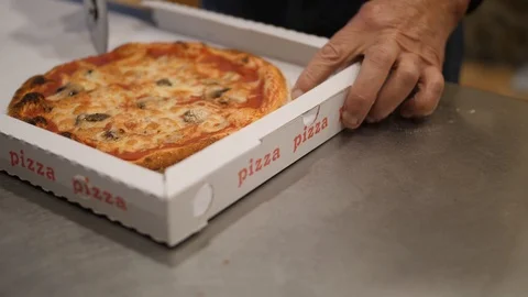 Man cuts pizza in box with wheel cutter. Close up shot of hands and takeaway Stock Footage 100743406